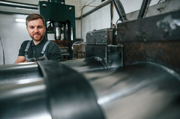 Holding part of metal construction. Man in uniform is in workstation developing details of agriculture technique