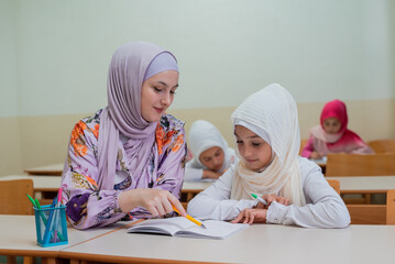 Female hijab Muslim teacher helps school children to finish the lesson in the classroom.	