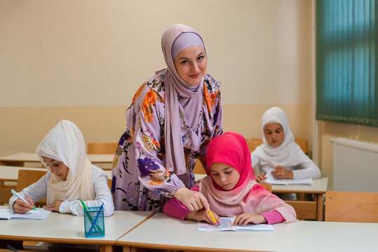 Female Hijab Muslim Teacher Helps School Children To Finish The Lesson In The Classroom.	