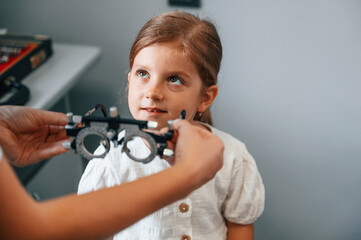 In special device with lenses. Little girl have their vision checking in the clinic by help of the female doctor