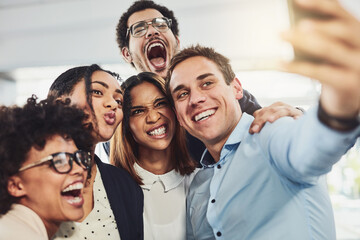 Teamwork, playful and selfie while a group of cheerful businesspeople making funny faces together for a social media post. Faces of a happy and fun team standing together in a creative office
