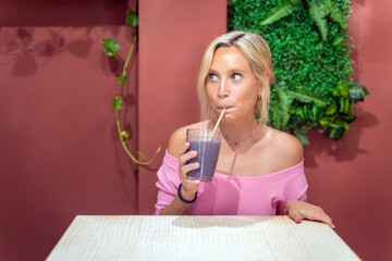 Young woman looking away while enjoying drinking a delicious smoothie in a coffee shop. Healthy lifestyle concept.