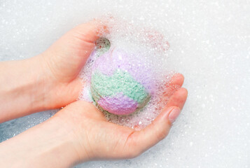 Fototapeta premium Female hands hold a bath bomb against the background of foam close-up.