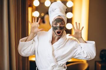 Woman with black mask on face in bathrobe in bathroom