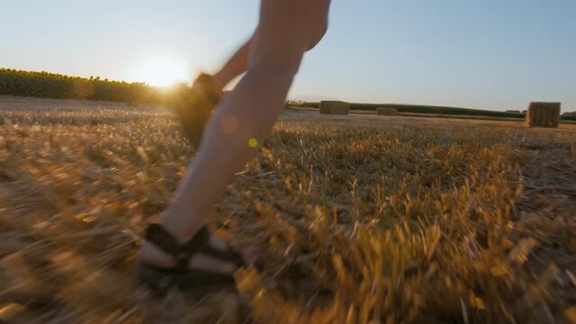 Camera follows feet of young skinny woman run away in field. Summer outdoor lifestyle freedom. Authentic and real feeling of happiness. Wide angle shot of happy woman run free at sunset