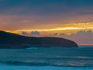 Fototapeta premium Cloud covered sunrise seascape and headland in soft pastel shades