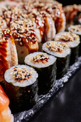 Close up of maki sushi with tuna, sauce and sesame seeds lying on the edge of a black stone plate.