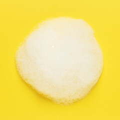 White fluffy foam on a yellow background. Top view.