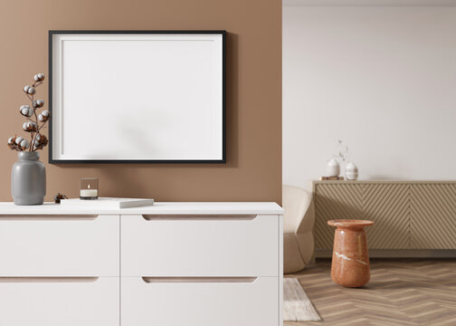 Empty black horizontal picture frame on brown wall in modern living room. Mock up interior in contemporary style. Free, copy space for your picture, poster. Sideboard, vase, cotton plant. 3D render.