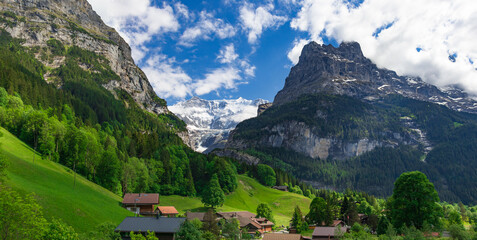 Fototapeta na wymiar Breathtaking panoramic view of the snowy slopes of the Alps and bright green slopes in the Alpine village of Grindelwald