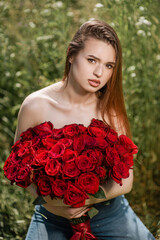 A beautiful girl poses in a field of flowers with a bouquet of red roses