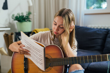 teenager reading songbook and playing acoustic guitar at home