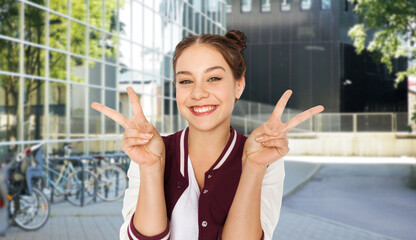 people, gesture and education concept - happy smiling teenage girl showing peace signs over city street or school yard background