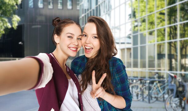 people and friendship concept - happy smiling pretty teenage girls taking selfie and showing peace sign over city street or school yard background