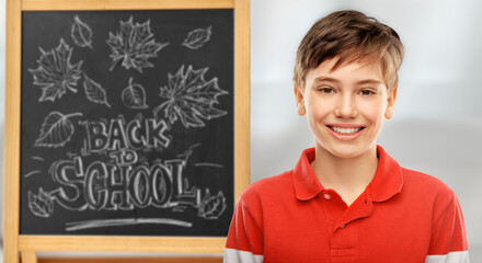 education, school and people concept - portrait of happy smiling student boy in red polo t-shirt over chalkboard on background