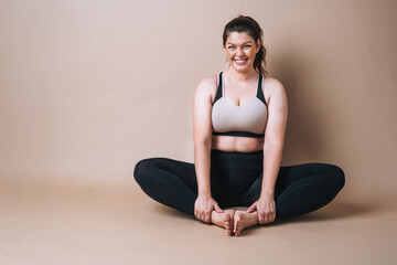 Self loving young woman plus size in sport wear doing stretching on beige background, body love