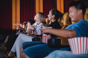 Group of audiences is watching a movie gleefully and bring food to eat while watching in the cinema.