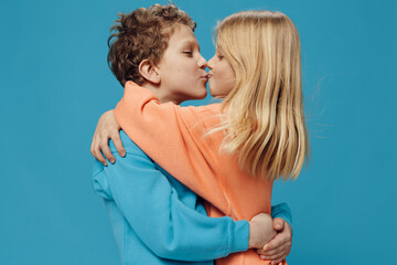 cute, joyful, loving children of school age stand on a blue background and kiss each other embracing