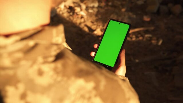 kharkiv, Ukraine, 02.8.2022, close-up, a soldier in camouflage uniform holds a smartphone with a vertical green screen in right hand,  chroma key smartphone technology