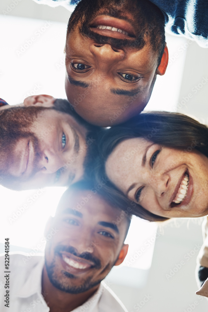 Poster Portrait of a diverse group of happy office workers from below joining together in a huddle for support and unity with lights in the background. Cheerful motivated colleagues ready for business