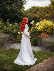 Fantasy photo red-haired woman walks in summer blooming garden. Long flowing red hair white vintage...
