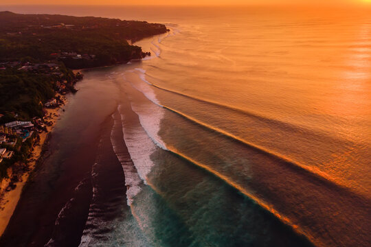 Aerial view of coastline and surfing waves at warm sunset. Perfect swell lines in Bali