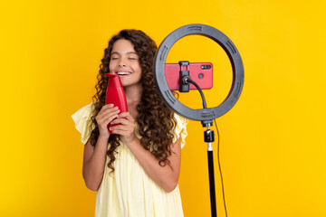 Teen girl hold hair conditioner or shampoo bottle in front of camera for vlog isolated on yellow...