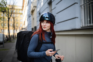 Female courier on bicycle with thermal backpack on way to deliver food to customers.