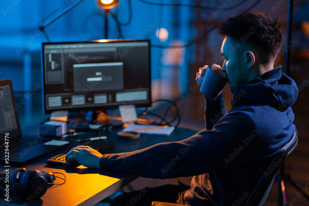 Poster cybercrime, hacking and technology concept - male hacker in dark room drinking coffee and using comp