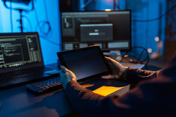 cybercrime, hacking and technology concept - close up of male hacker in dark room with tablet pc using computer virus program for cyber attack