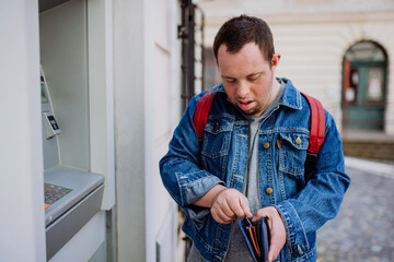 Happy young man with Down sydrome using a street ATM machine and withdrawing money.