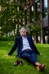 Naklejka na ściany i meble Mature businessman resting and sitting barefoot in park, feeling free, escaping from work, work life balance concept.