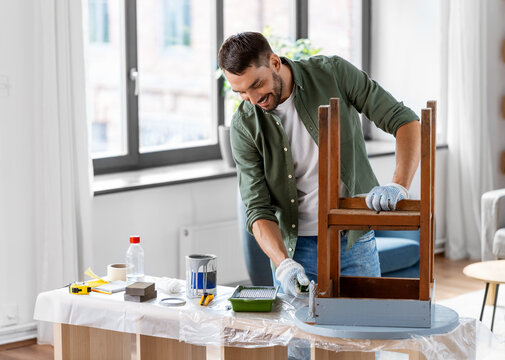 renovation, diy and home improvement concept - man in gloves with paint roller painting old wooden table in grey color