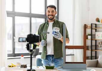 blogging, furniture restoration and home improvement concept - man or blogger with camera repainting old wooden table with paint roller in grey color and recording tutorial video