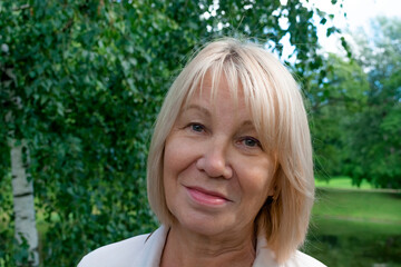 Portrait of a 50-60-year-old woman on a natural green background. Blonde hair, open eyes. Outdoor recreation creates a good mood