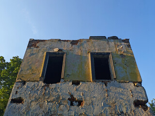The facade of an old building that is collapsing against the blue sky. Broken windows of an old house