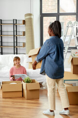 moving, people and real estate concept - women unpacking boxes at new home