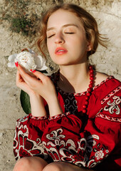 A beautiful girl in a traditional ethnic red dress posing outdoors with a white peony flower in her...