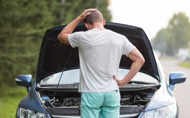 A man stands near the open hood of a car. The car needs repair