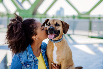 Multiracial girl sitting and resting with her dog outside in the bridge, , spending leisure time together. Concept of relationship between dog and teenager, everyday life with pet.