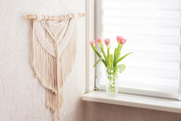 Handmade macrame. 100% cotton wall decoration with wooden stick hanging on a white wall.   Macrame braiding and cotton threads.  Female hobby.  ECO friendly modern knitting concept in the interior