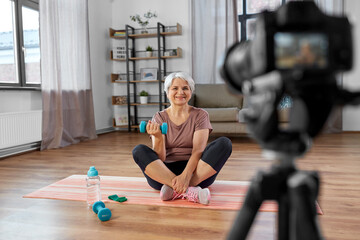fitness, sport and video blogging concept - happy senior woman or blogger with camera and dumbbell...