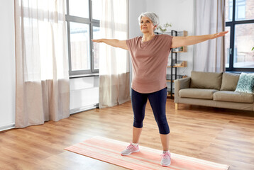 sport, fitness and healthy lifestyle concept - smiling senior woman exercising on mat at home