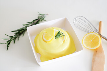 Round minimal fresh, sweet, sour and tasty Lemon chiffon or sponge cake. top with lemon sauce. Decorated with rosemarry, whisk, paddle and lemon slice in a white background. Use for minimal cafe.