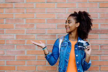 Multiracial girl standing in front of brick wall with camera, and posing.