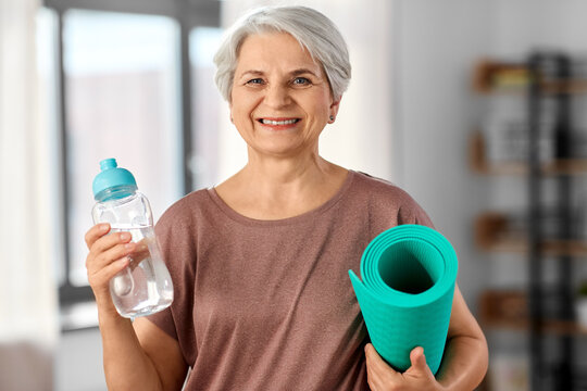 sport, fitness and healthy lifestyle concept - smiling senior woman with yoga mat and bottle of water at home