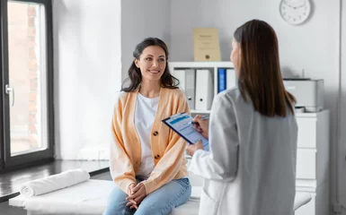 medicine, healthcare and people concept - female doctor with clipboard talking to smiling woman patient at hospital © Syda Productions