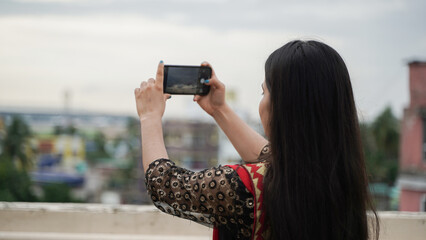Beautiful Indian woman taking photo with her mobile phone camera, young female Asian photographer
