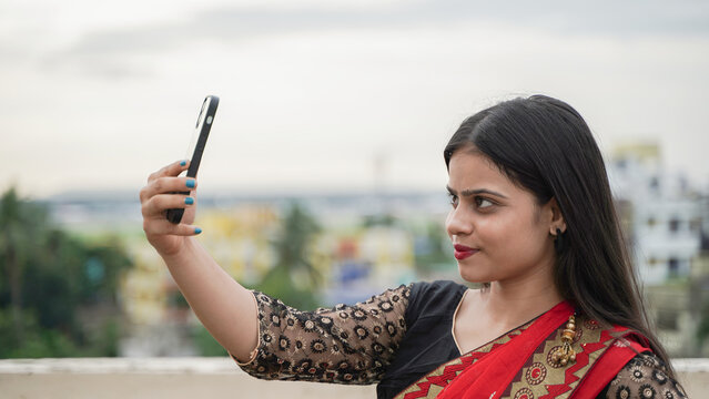 Beautiful Indian girl taking selfie on her mobile phone outdoor, cheerful Asian woman in traditional dress clicking selfie