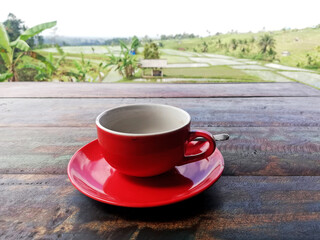 Black coffee on red color cup,placed on wooden table,with rice field background